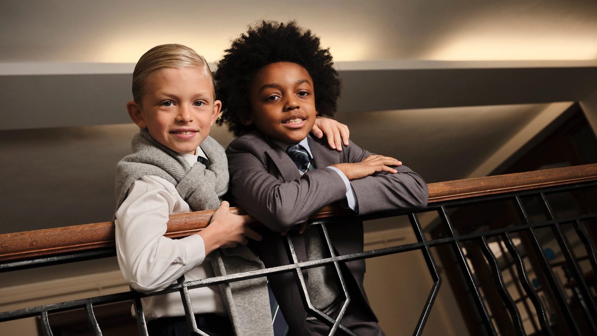 Two students in grey school uniforms leaning together on a staircase railing