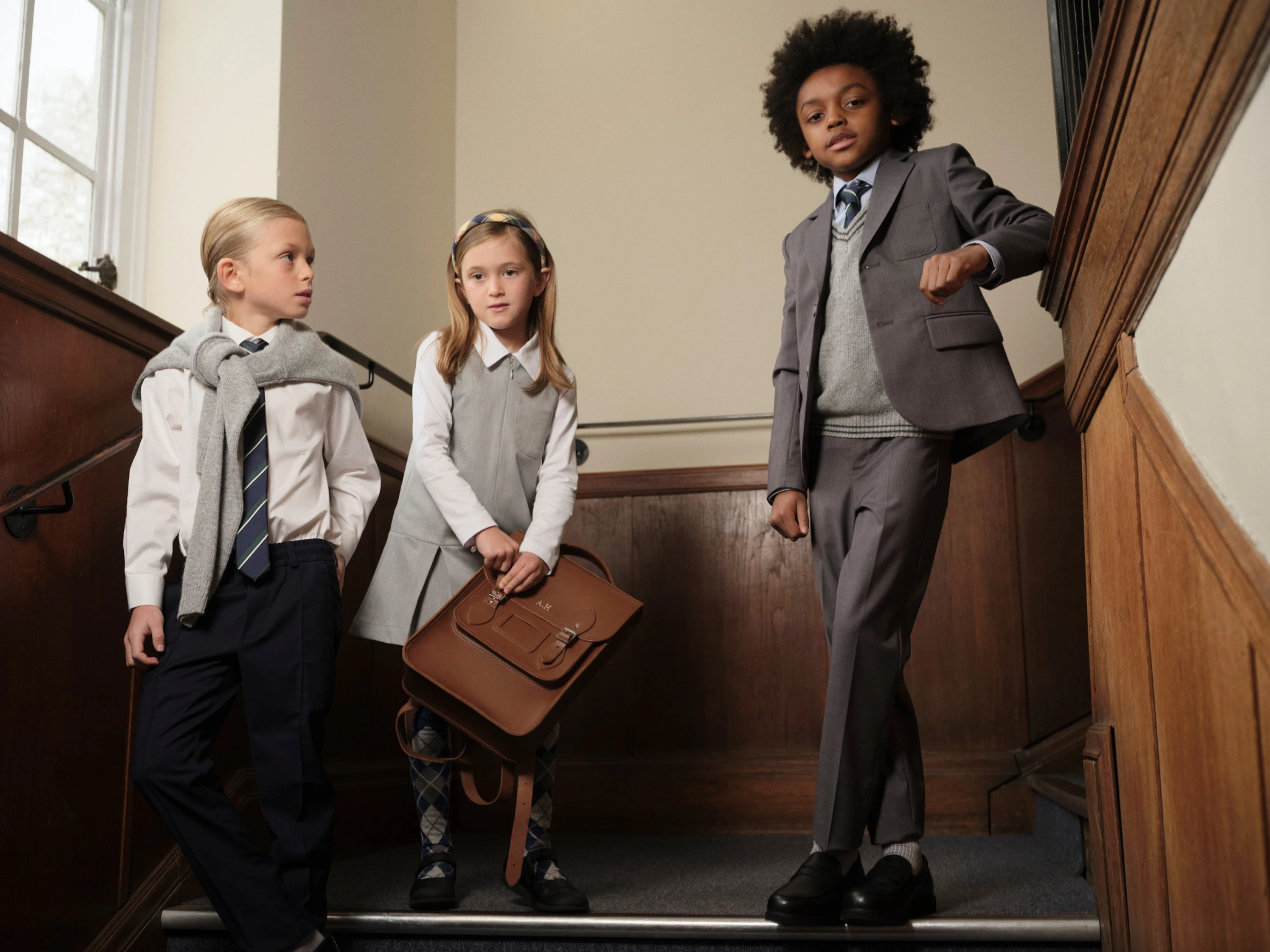 Three students in grey school uniforms standing on a wooden staircase